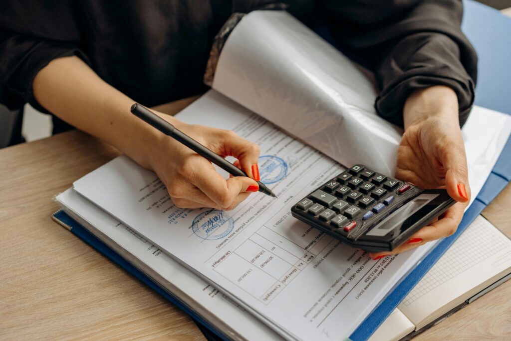 pexels-photo-8296977-8296977 An accountant using a calculator and signing paperwork, showcasing financial analysis.